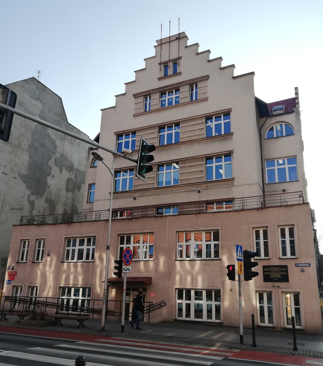 Budynek z 5 piętrami. Przed budynkiem przejście dla pieszych i sygnalizacja świetlna.
