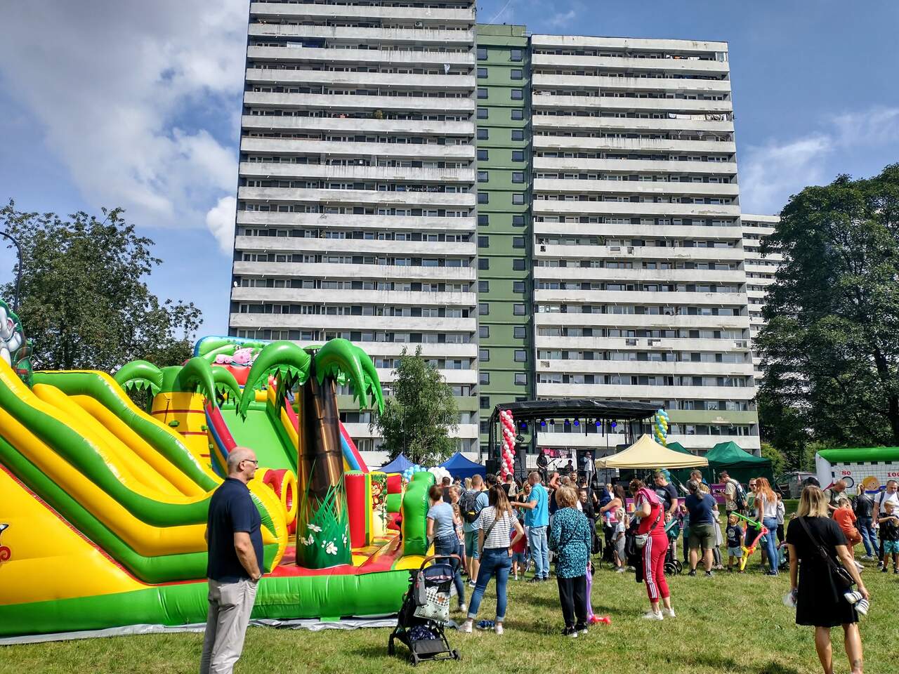 Zdjęcie przedstawia dmuchańce dla dzieci, które znajdują się na tle blokowiska. Wokół dmuchańców znajdują się dorośli i dzieci.