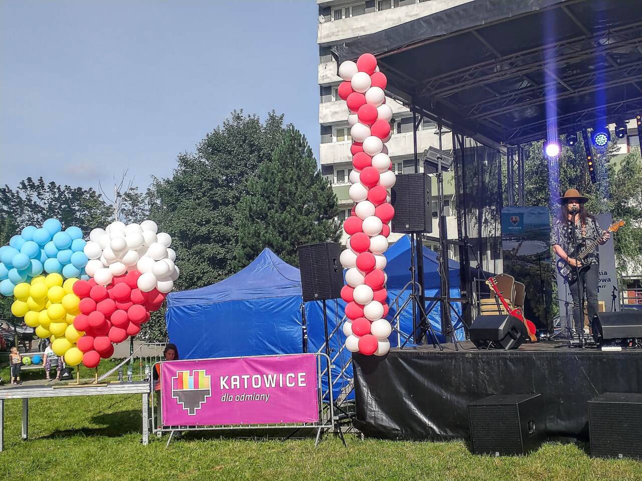  niebieski, żółty, biały i czerwony. Na scenie występuje wokalista w długich włosach, gra na gitarze.